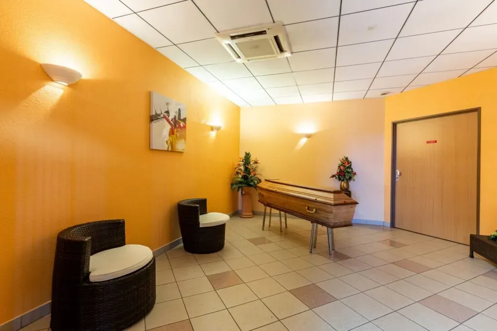 Chambre funéraire lumineuse aux murs orange avec cercueil et fauteuils en résine.