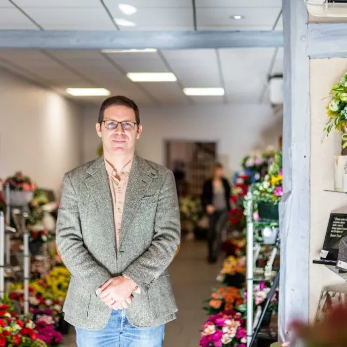 Homme en costume souriant se tenant debout dans un magasin de fleurs funéraires.
