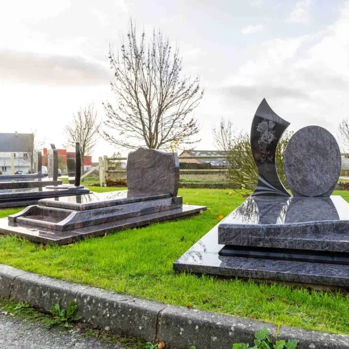 Allée de monuments funéraires en granit exposés dans un cimetière paysager.