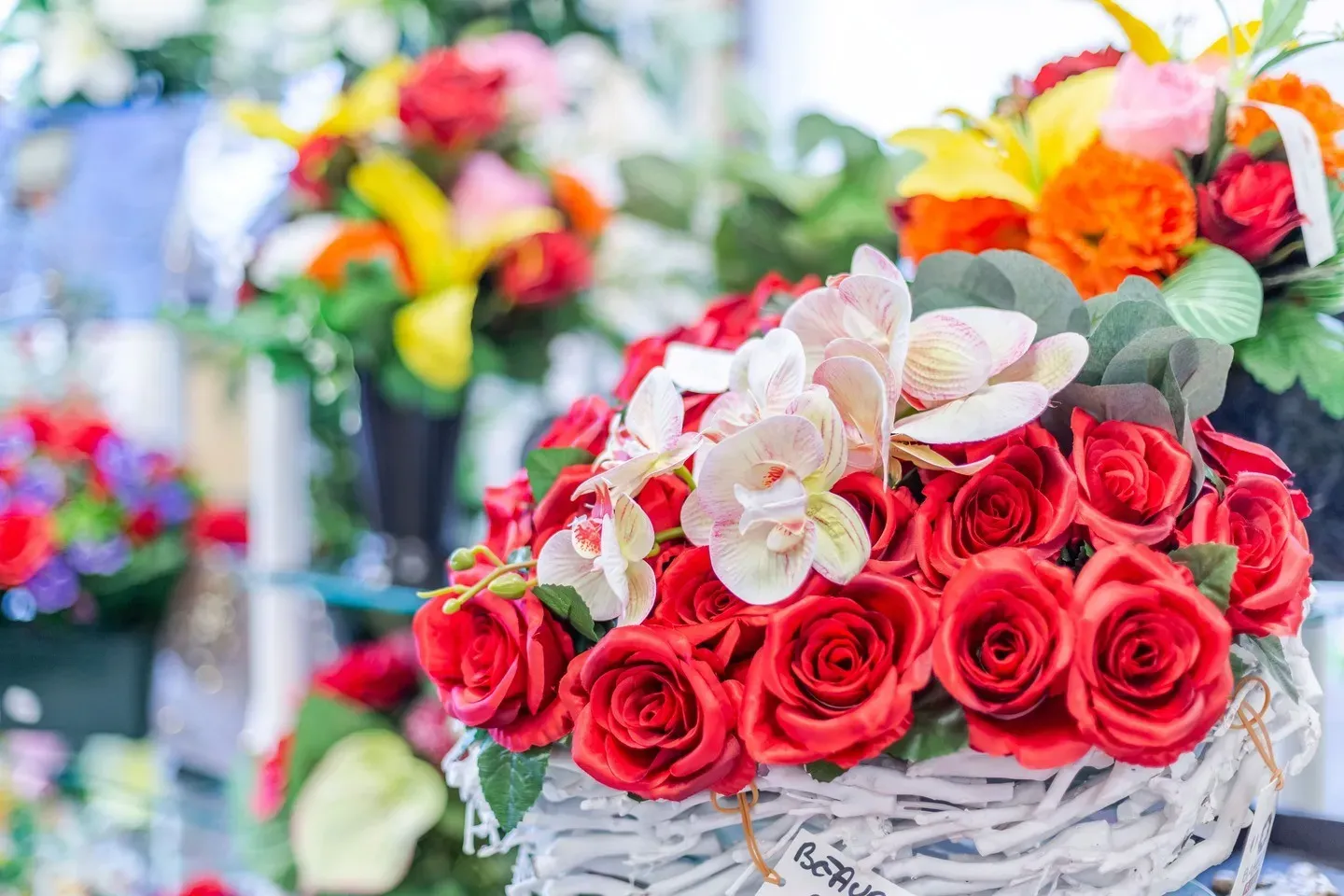 Coupe florale funéraire de roses rouges et d'orchidées blanches en panier tressé.